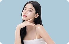 Młoda kobieta o długich czarnych włosach pozująca na jasnoniebieskim tle, prezentująca zdrową i lśniącą cerę.