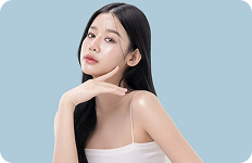 Młoda kobieta o długich czarnych włosach pozująca na jasnoniebieskim tle, prezentująca zdrową i lśniącą cerę.