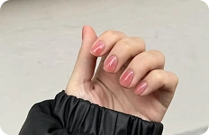 Zbliżenie na dłoń z krótkimi paznokciami pomalowanymi na lśniący, brzoskwiniowo-różowy kolor.